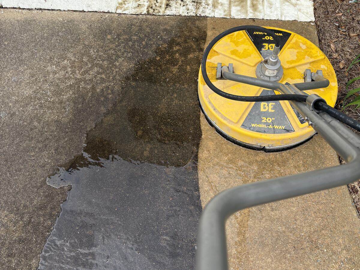 A twenty-inch surface cleaner mid-pass, with a sharp line between the dirty concrete and the cleaned strip behind it