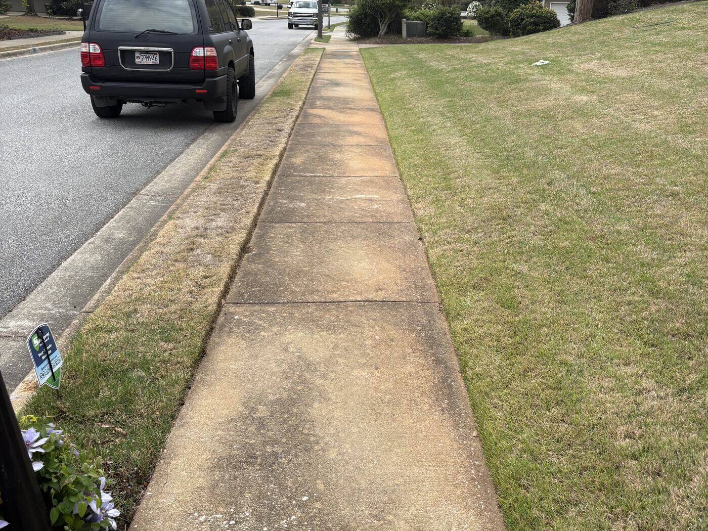 The same sidewalk before pressure washing, darkened with dirt and organic staining