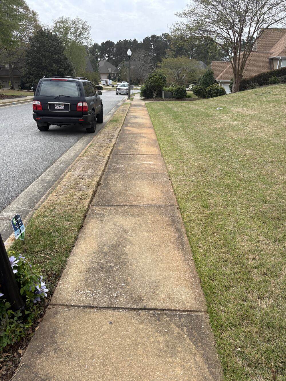 The same neighborhood sidewalk before cleaning, streaked and darkened along the curb